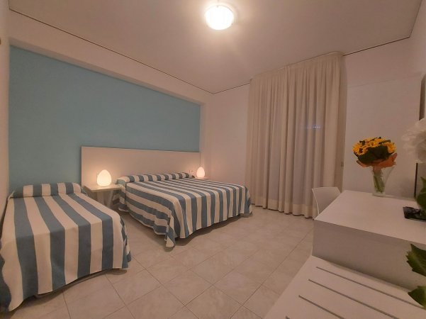 Camera da letto con tre letti a righe blu e bianche, tende lunghe e decorazione floreale.