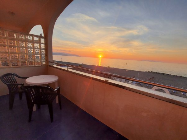 Balcone con due sedie e un tavolo, vista tramonto sul mare.