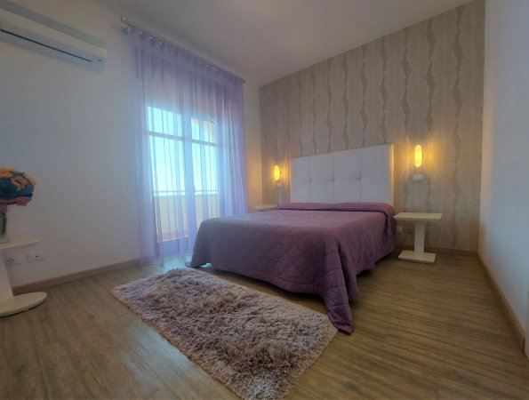 Camera da letto con letto viola e tende trasparenti, luce calda.