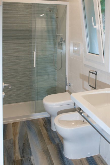 Bagno moderno con doccia in vetro, WC e bidet su pavimento effetto legno.