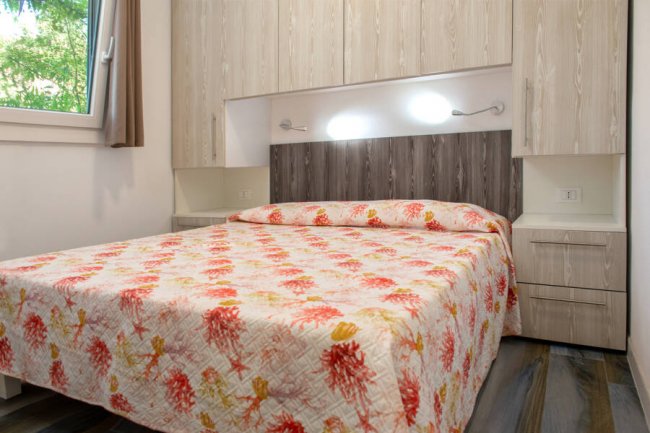 Camera da letto con letto matrimoniale e copriletto colorato, armadi sopra il letto.