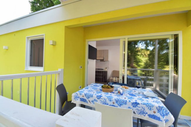 Terrazza gialla con tavolo apparecchiato e sedie, vista su un giardino verde.