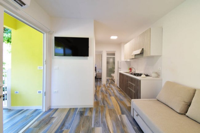 Soggiorno con cucina, pavimento in legno multicolore, TV a parete e divano beige.