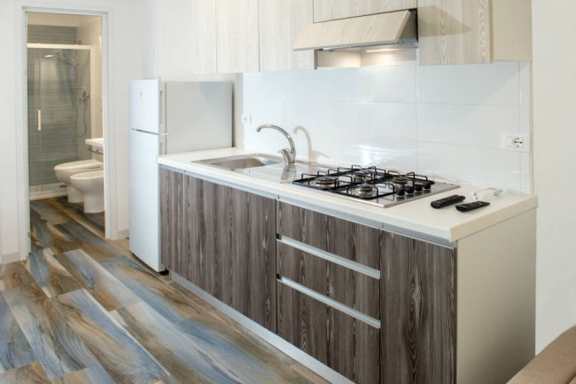 Cucina moderna con pensili in legno scuro, piano cottura e lavello. Bagno sullo sfondo.