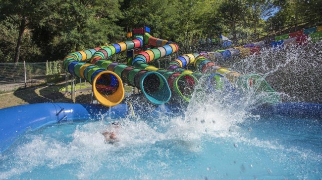 Scivoli d'acqua colorati con gente che si tuffa in piscina, creando grandi schizzi.