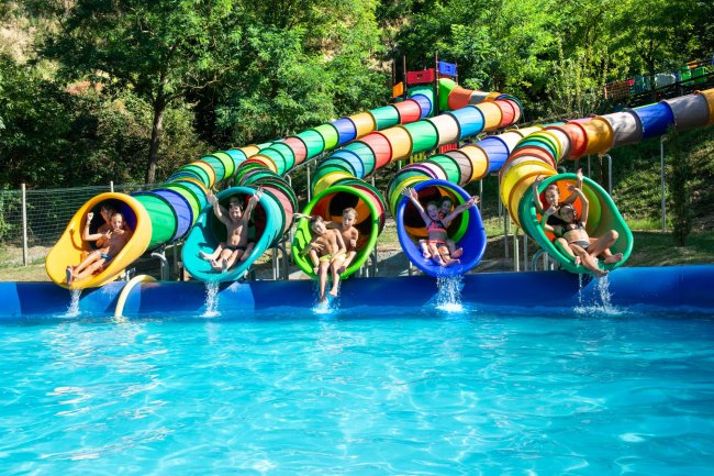 Cinque persone che escono da scivoli d'acqua colorati, atterrando in piscina.
