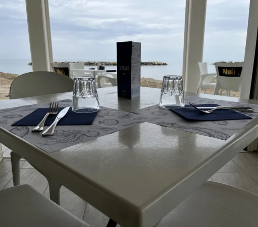 Tavolo apparecchiato per due in un ristorante con vista sul mare.