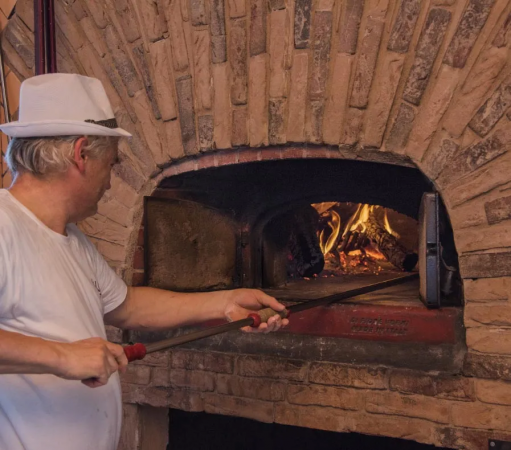 Uomo con cappello bianco inforna in un forno a legna di mattoni.