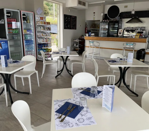 Interno di bar moderno con tavoli apparecchiati e frigoriferi visibili.