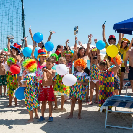 Gruppo di bambini e adulti in costumi colorati con palloncini su una spiaggia.