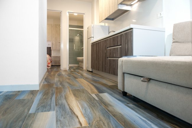 Un appartamento con pavimento effetto legno, cucina moderna e divano beige.
