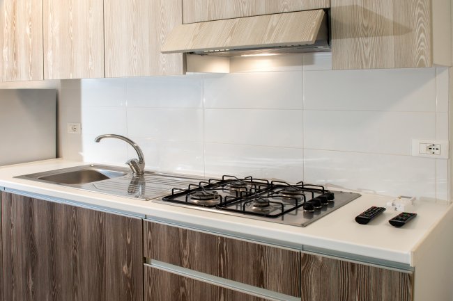 Cucina con lavello acciaio, fornelli a gas, e mobili in legno chiaro.