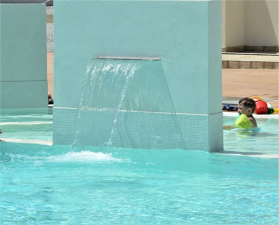 Bambino con braccioli verdi in una piscina vicino a una cascata d'acqua artificiale.