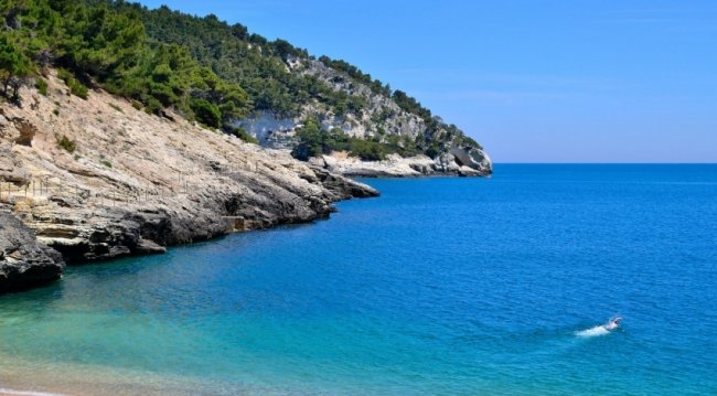 Scogliera rocciosa su mare blu, una persona nuota.