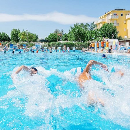 Due persone nuotano in una piscina affollata.
