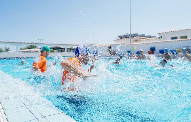 Persone giocano in piscina con schizzi d'acqua.