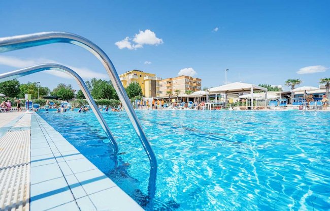 Bordo piscina con ombrelloni e edifici sullo sfondo.