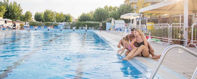 Famiglia seduta a bordo piscina, con i piedi nell'acqua.