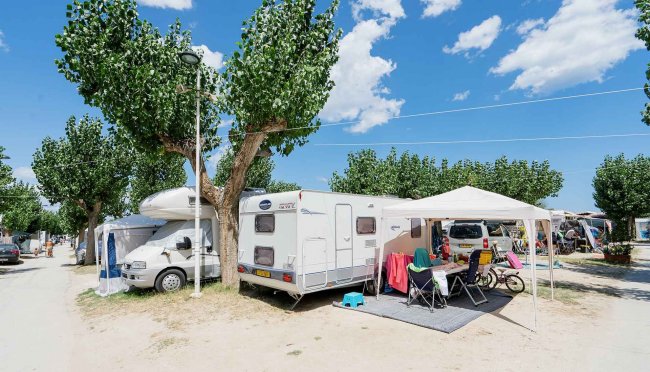 Caravan e tenda sotto gli alberi in un campeggio.