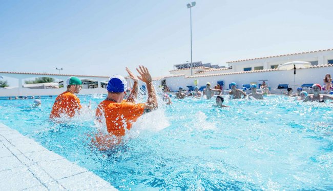 Persone in piscina giocano a pallanuoto, indossando caschi colorati.