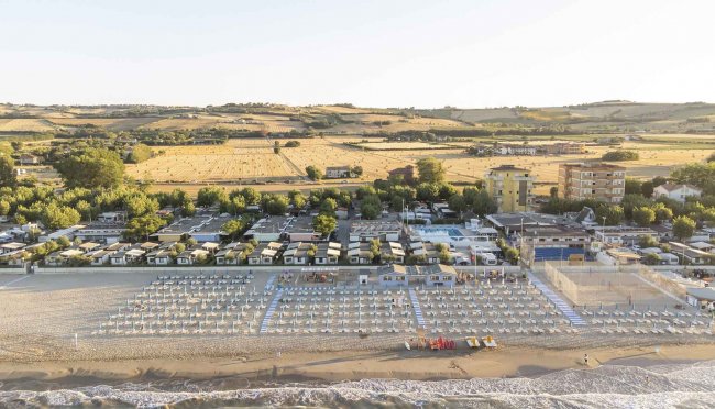 Spiaggia con ombrelloni e file di sedie a sdraio vicino a campi agricoli.