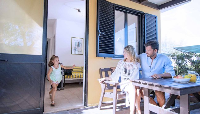Bambina che corre verso due adulti seduti su una patio.
