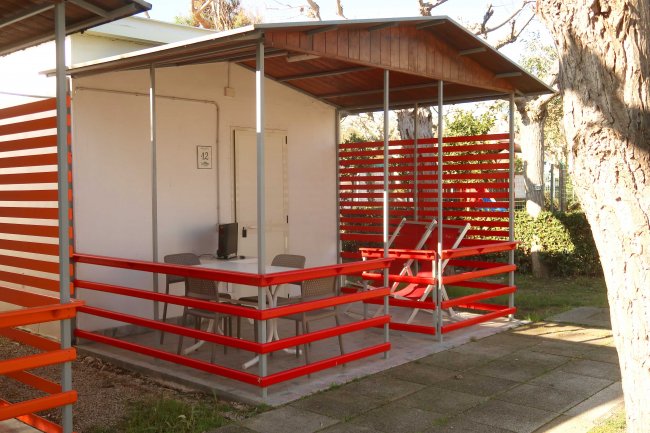 Portico con sedie e tavolino, recinzione rossa e tetto spiovente.