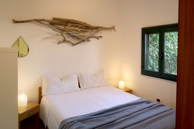 Letto matrimoniale bianco con decorazioni di legno sulla parete e una finestra verde a lato.