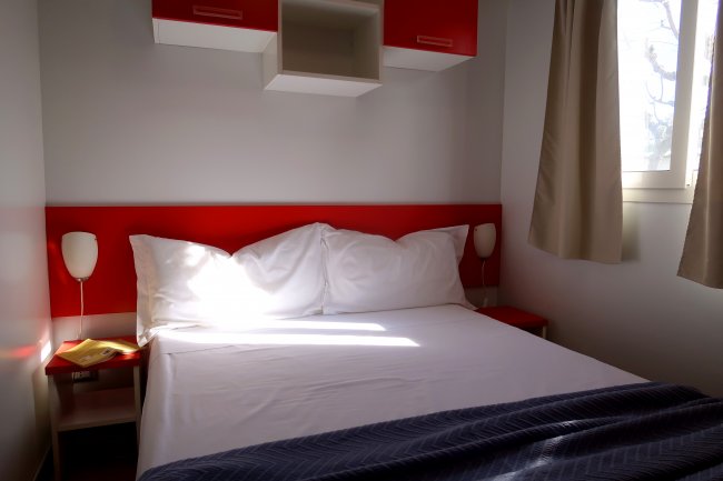 Un letto matrimoniale con testiera rossa e cuscini bianchi, luce naturale.
