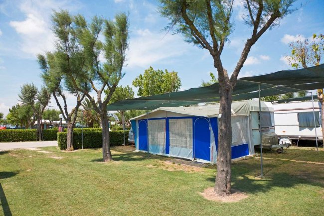 Caravan bianco e blu sotto alberi e tenda.