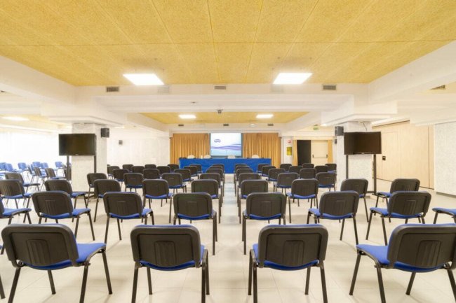 Sala conferenze con sedie blu e schermo davanti.