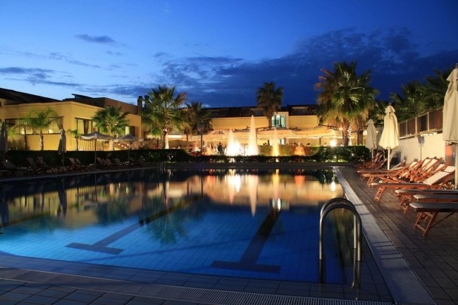 Piscina illuminata di notte con sedie a sdraio.