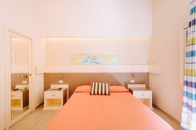 Letto singolo con copriletto arancione e comodini.