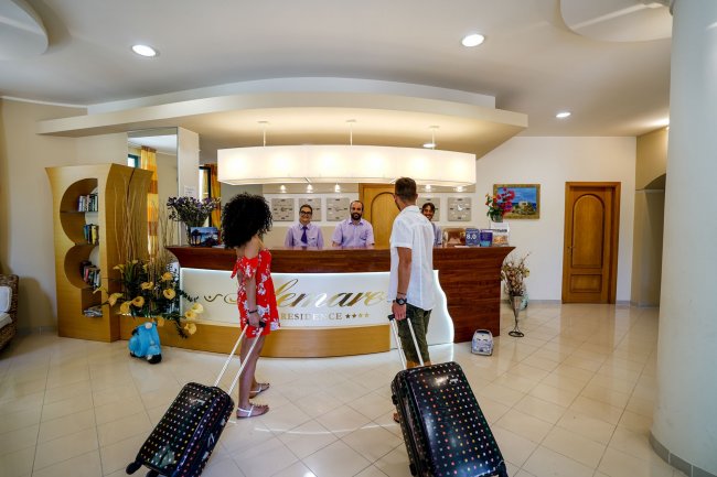 Due persone con valigie alla reception di un hotel.