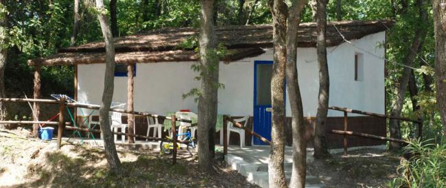 Casetta bianca tra alberi con sedie e tavoli esterni.
