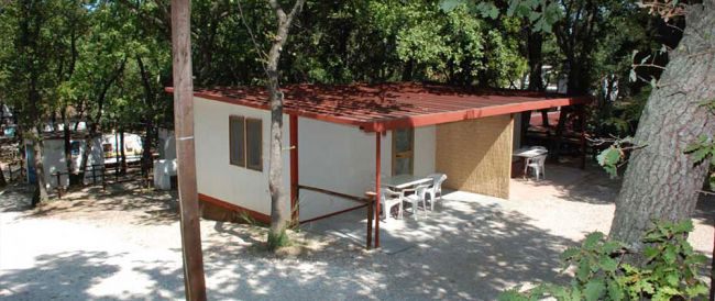 Casa prefabbricata circondata da alberi e sedie all'esterno.
