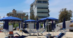 Spiaggia con ombrelloni blu davanti a edifici.
