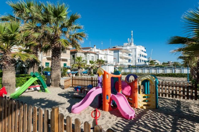 Area giochi per bambini sulla sabbia con palme.