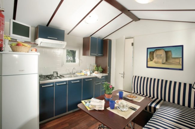 Piccola cucina con tavolo, sedie a righe, e armadietti blu.