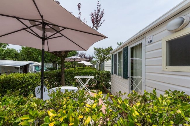 Veranda con ombrellone e sedie, circondata da siepi.