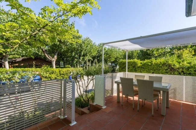 Terrazza con tavolo, sedie e pergolato, circondata da piante verdi.