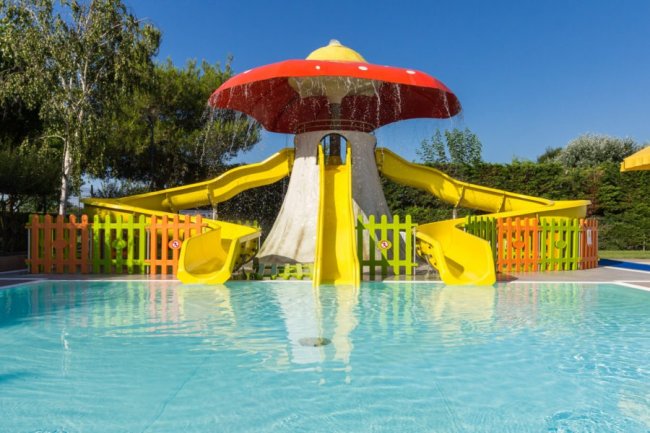 Scivoli gialli sotto un fungo spruzzante in una piscina per bambini.