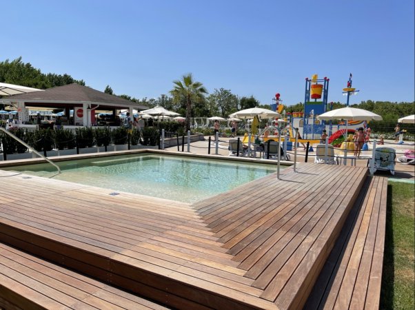 Piscina con bordo in legno vicino a un'area giochi acquatica.
