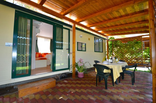 Tavolo apparecchiato sotto una veranda di fronte a una roulotte.