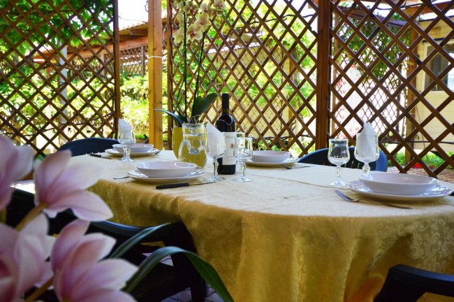 Tavolo apparecchiato all'aperto con grata e fiori.