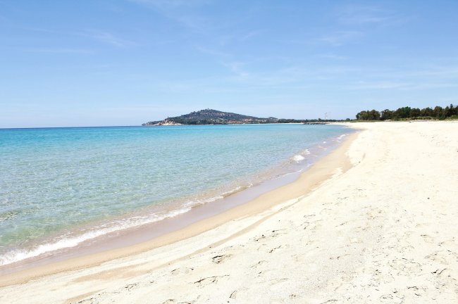 Spiaggia sabbiosa con mare turchese e colline in lontananza.