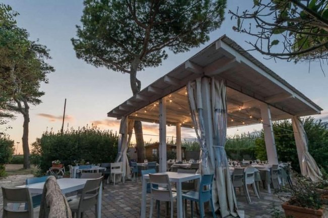 Terrazza all'aperto con tavoli e sedie sotto un tetto illuminato.