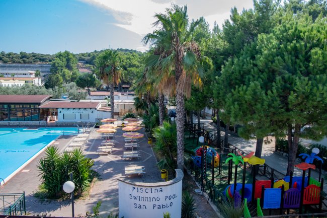 Piscina con palme e area giochi per bambini.
