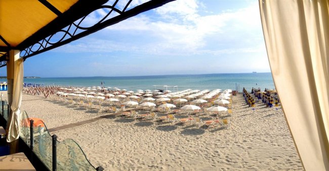 Spiaggia con file di ombrelloni bianchi e vista mare.