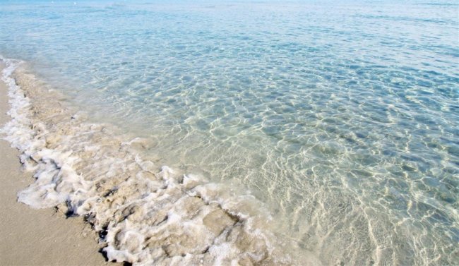Acqua cristallina che lambisce la riva sabbiosa.
